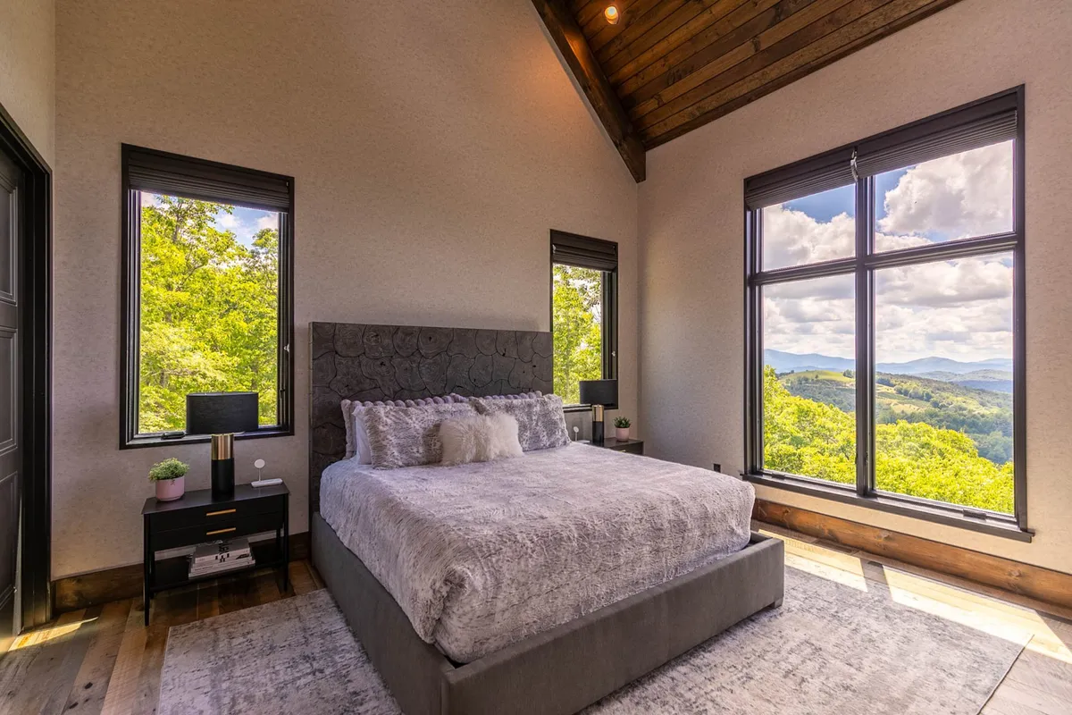 A spacious bedroom featuring a large bed positioned to enjoy a breathtaking mountain view through expansive windows. Nightstands with elegant lamps frame the bed, and the serene atmosphere is complemented by soft, neutral tones and an uncluttered design.