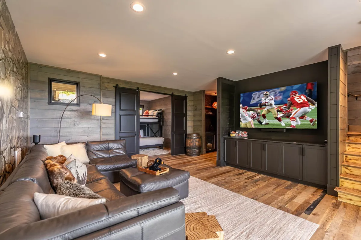 A comfortable den with a large TV screen, plush leather sectional couch, and a warm, relaxed atmosphere. The setup is perfect for movie nights or casual gatherings.