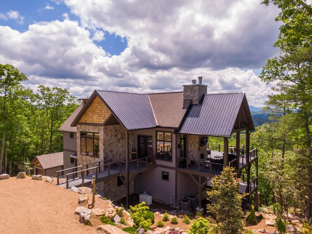 The home’s stone and wood facade opens onto an expansive deck set amid mature trees and mountain scenery. The elevated position offers a panoramic outlook, inviting guests to relax, socialize, or simply take in the natural beauty after a day on the trails.