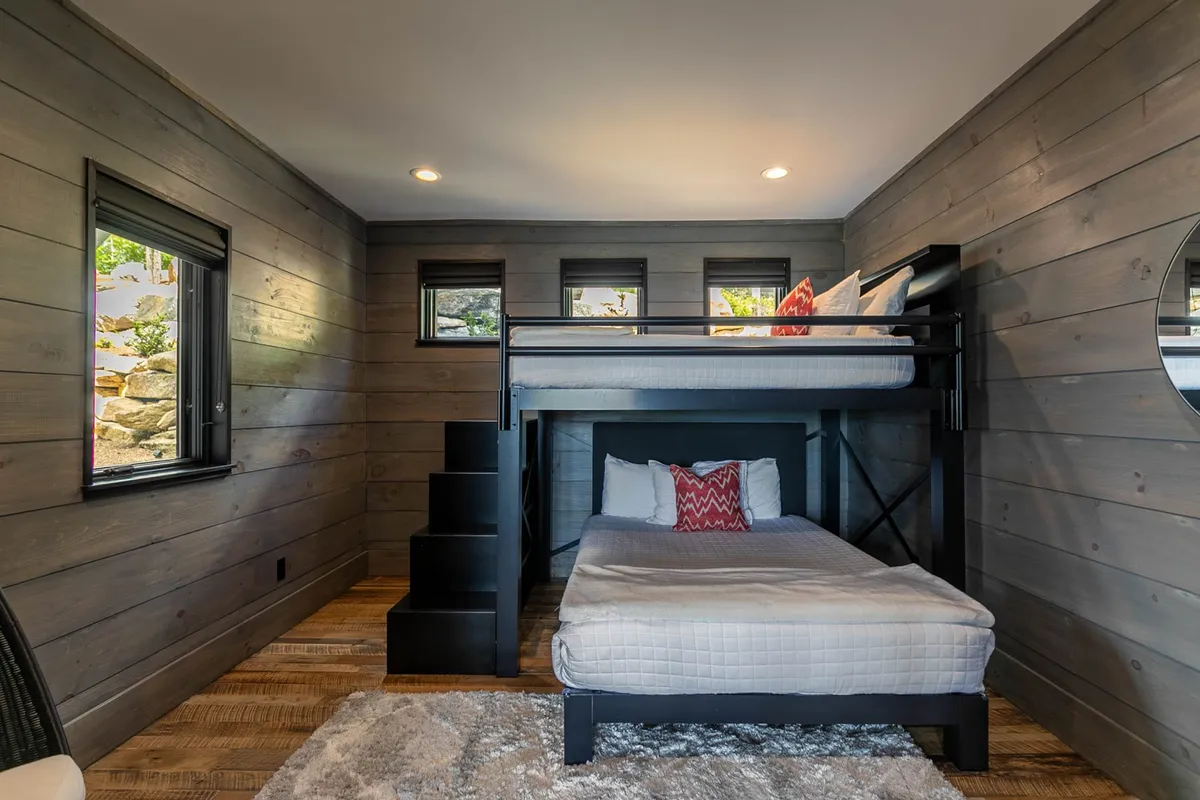 A playful, cozy bunk room featuring a queen-over-queen bunk bed, textured accent walls, and a soft rug. The space is designed for comfort and fun, making it ideal for families or groups with children.