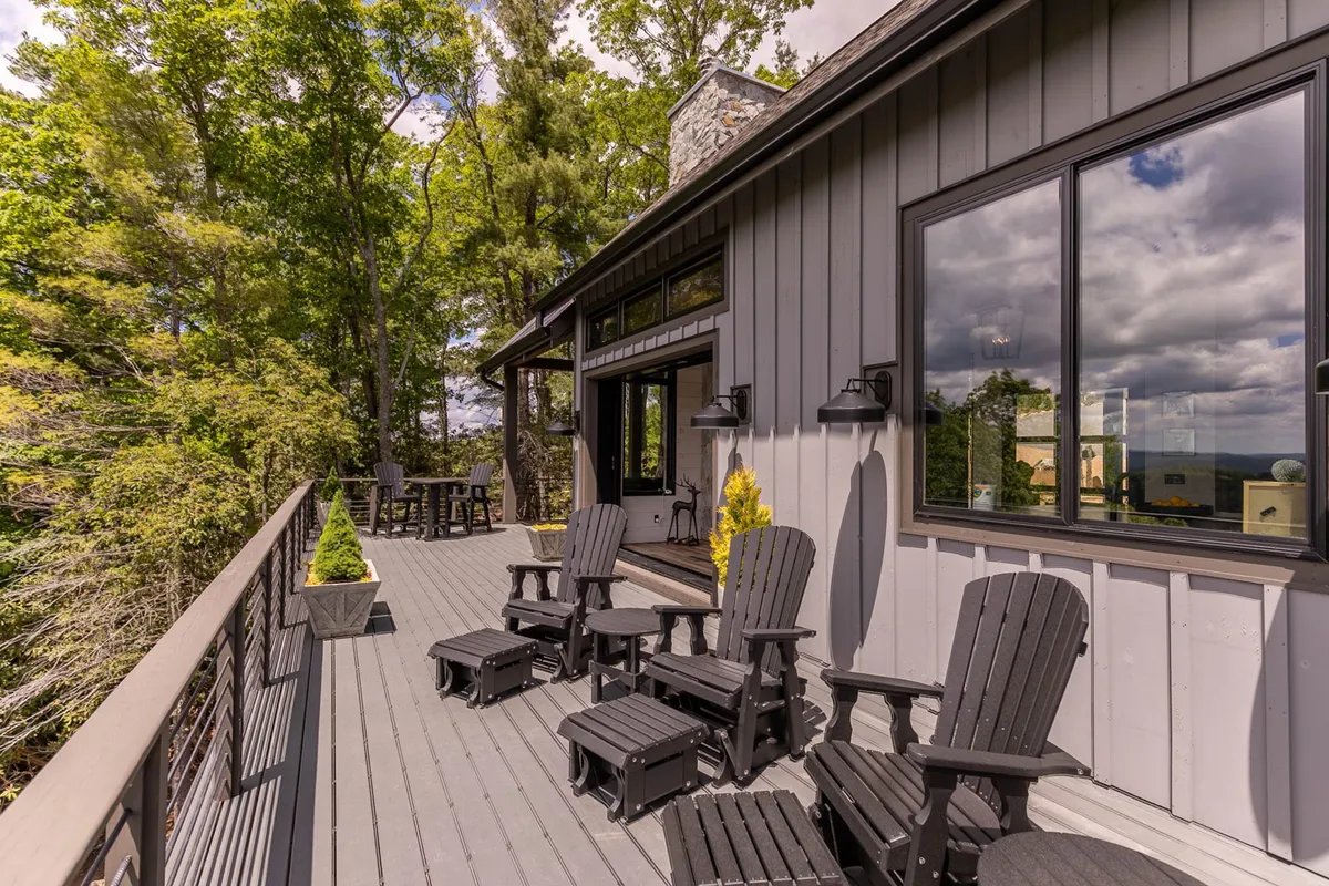 An inviting deck area with comfortable chairs, wooden railing, and surrounding trees, with large windows in the background. The scene is peaceful yet social, ideal for relaxing and enjoying nature while staying close to all the amenities.