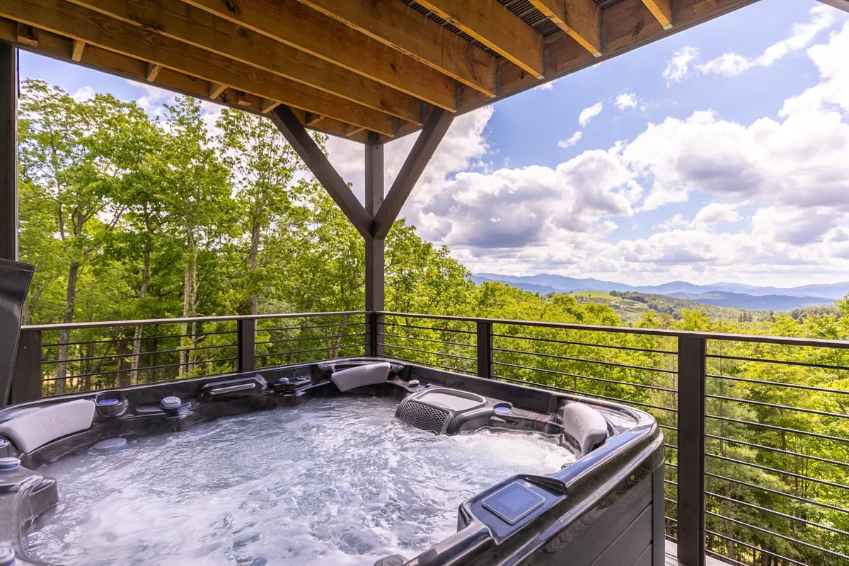 This image showcases an outdoor hot tub positioned under a wooden pergola, with a stunning mountain view in the background. The setting is serene, inviting guests to relax and enjoy nature, whether soaking at sunrise or stargazing after dark.