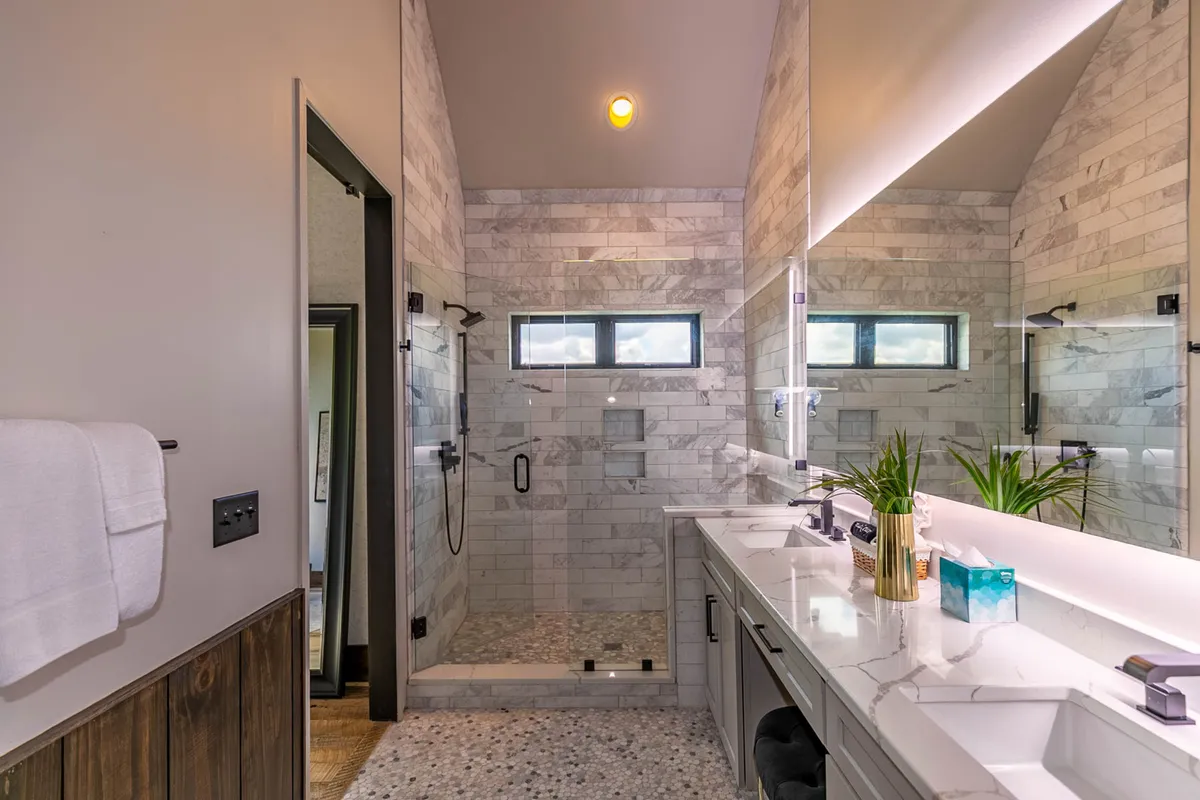 A spa-inspired bathroom with a double marble vanity and a large walk-in tiled shower. Natural light streams in from the windows, highlighting the elegant fixtures and clean, modern lines.