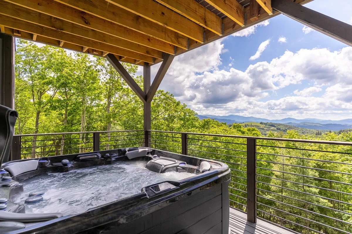 An elegant exterior scene showcasing a private hot tub on a covered deck with panoramic views of the surrounding mountains. The wooden ceiling and open design allow for relaxation in a serene natural setting, making it a perfect place to unwind after a day of wine tasting or fine dining.