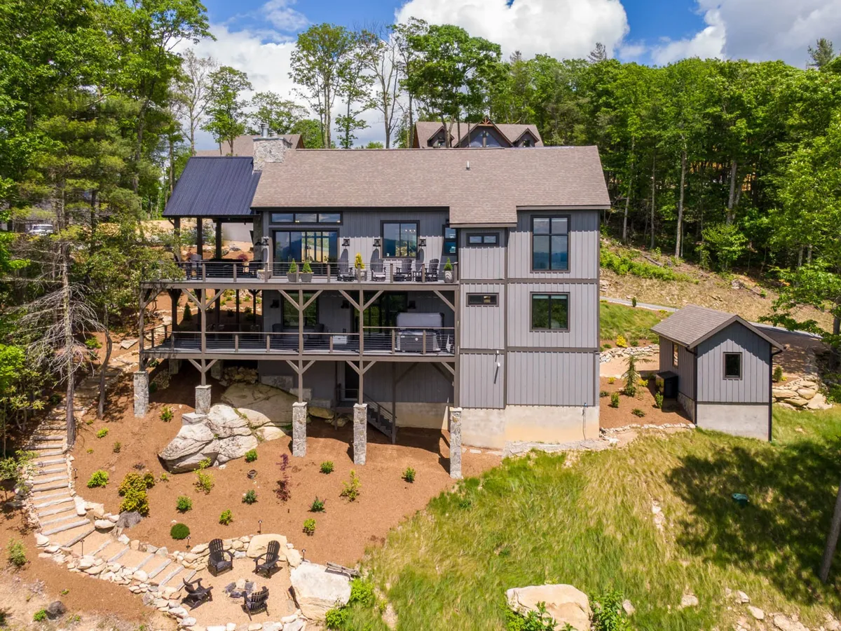 A multi-level deck extends from a stately home, surrounded by lush greenery and a well-landscaped garden. Ample outdoor seating, a fire pit, and open space invite gatherings, relaxation, and enjoying expansive mountain views. The setting reflects both adventure in the nearby wilderness and comfort at home.