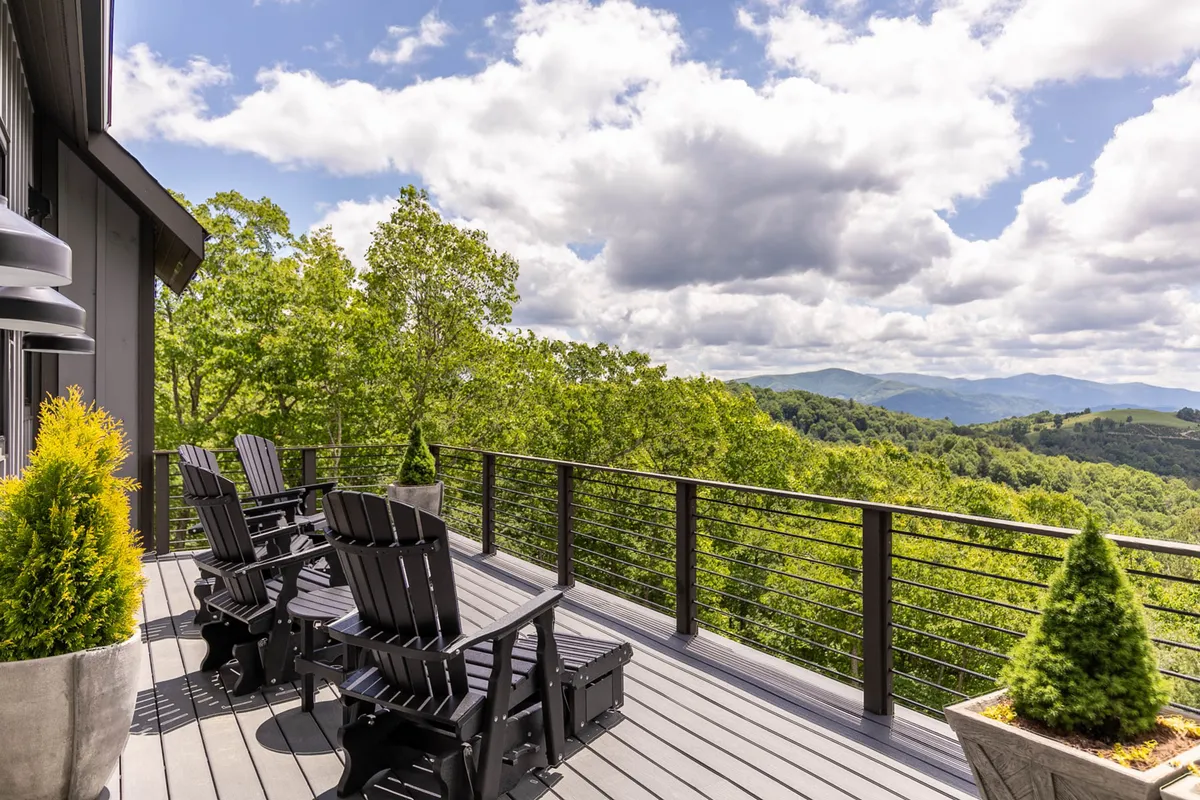 An exterior view of a deck furnished with black Adirondack chairs, surrounded by lush greenery and offering striking mountain views. The setting is calm and inviting, ideal for enjoying a glass of wine at sunset or relaxing with friends after an upscale meal.